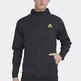 Cortavientos deportivo Le Coq Sportif, color negro, con capucha y cierre frontal. Presenta el logo del gallo en amarillo neón en el pecho izquierdo. El tejido es ligero y arrugado, típico de cortavientos.