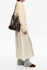 Bolso de hombro tipo tote de Bimba y Lola, confeccionado en piel vacuna con acabado brillante. Presenta un diseño estructurado con asa larga decorada con tachas metálicas plateadas y cierre de botón a presión.