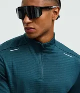 Remera deportiva de manga larga con cuello alto y cierre frontal parcial. Presenta una textura acanalada en toda la prenda y detalles reflectivos en los hombros.