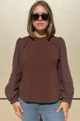 Remera de color marrón con cuerpo de algodón y mangas largas de tela texturizada. Presenta cuello redondo con frunce y elástico, y puños elásticos.