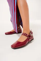 Balerinas color borgoña de charol con punta cuadrada, correa con hebilla y apliques metálicos.