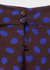 Blusa sin mangas de corte recto con cuello drapeado y cierre de botones. Presenta un diseño estampado de lunares en color azul sobre fondo oscuro.