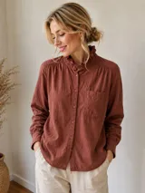 Camisa de manga larga color terracota con cuello alto tipo mao con volados, cierre frontal con botones y bolsillo en el pecho.