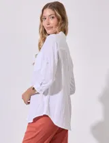 Camisa blanca de corte clásico con textura de líneas verticales, cuello con solapa, cierre frontal con botones y bolsillo en el pecho. Presenta mangas tres cuartos regulables con presilla y botón.