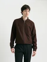 Campera tipo bomber de color marrón, confeccionada en tejido con textura similar a la gamuza, con cierre frontal completo, cuello redondo y puños elásticos.