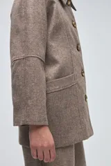 Chaquetón de lana fina sin teñir, con cuello camisero, cierre frontal de botones y bolsillos delanteros. Diseño de corte recto y estructura clásica.