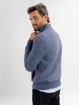Campera tejida de punto jaspeado en tono azul, con cierre frontal completo, cuello alto y detalles de ribete en color marrón en los bolsillos y a lo largo del cierre. Presenta puños y ruedo acanalados.