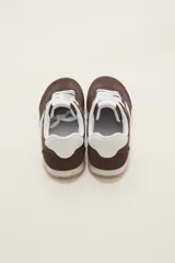 Zapatillas de estilo urbano color marrón con detalles en blanco, confeccionadas en material textil y sintético, con cordones blancos y suela de goma.