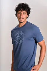 Remera de cuello redondo y manga corta, color azul, con estampado circular en el pecho que incluye el logo de la marca Original Penguin.
