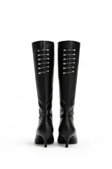 Botas altas de caña media en eco cuero negro, con taco fino de 4 cm y punta fina. Presentan un diseño distintivo en la parte posterior con una hilera de ganchos metálicos tipo imperdibles plateados.