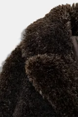 Abrigo corto de textura de pelo sintético, color marrón oscuro, con cuello de solapa, manga larga y cierre frontal con corchetes.