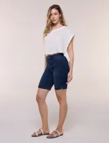 Bermuda de jean azul oscuro con calce ajustado y tecnología push up. Presenta cintura con presillas, cierre frontal con botón metálico, diseño clásico de cinco bolsillos y largo por encima de la rodilla con dobladillo en el ruedo.