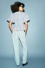 Top de cuello redondo con cuerpo de nido de abeja elástico y mangas cortas abullonadas con elástico en los puños. Presenta un diseño de rayas verticales en tonos azul, rojo y negro, con un bajo estilo peplum y cierre de botón en la espalda.