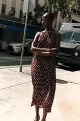 Vestido midi de cuello halter con tejido efecto arrugado y estampado de lunares blancos sobre fondo bordó. Presenta forro interior y cierre en la espalda con cremallera oculta y botones.