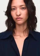 Vestido midi de corte evasé en color azul marino, con cuello camisero, cierre frontal de botones ocultos y mangas largas con puños abotonados. Incluye un cinturón fino ajustable con hebilla metálica.