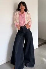 Jean de tiro alto con corte elefante, caracterizado por su silueta amplia y acampanada en las piernas. Confeccionado en denim de color azul oscuro con costuras a contratono.