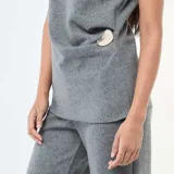 Sweater gris sin mangas confeccionado en tejido de punto, con cuello alto y detalle de hebilla metálica dorada en el lateral.