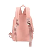 Mochila urbana Las Oreiro de color rosado, confeccionada en material sintético con acabado satinado. Presenta un compartimento principal con cierre, un bolsillo frontal con cierre, correas ajustables para los hombros y manijas superiores. Incluye un aplique metálico con forma de labios y un llavero decorativo con borlas de colores.