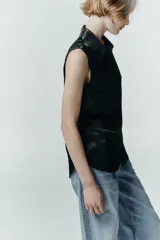 Camisa sin mangas de tejido satinado, con cuello solapa, cierre frontal con botones ocultos y bolsillos de plastrón con solapa en el delantero. Presenta un bajo asimétrico y corte recto.