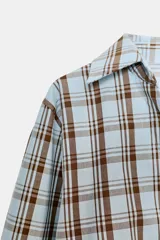 Camisa de algodón con estampado a cuadros en tonos celeste y marrón. Presenta cuello solapa, escote pico y diseño cruzado con lazada frontal.