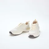 Zapatillas estilo running de color beige, confeccionadas con una combinación de paneles de cuero sintético y malla transpirable. Presentan cordones al tono, suela robusta con relieve y detalles en color marrón oscuro en la base.