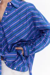 Camisa oversize de algodón con estampado de rayas multicolor en distintas direcciones, cuello camisero, mangas largas y detalle de botonera vertical en la espalda.