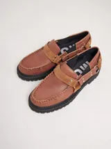 Mocasines Mutma Gales de cuero color tostado, con plataforma gruesa dentada, detalles de tachas metálicas, argollas y tira lateral con hebilla.