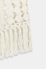 Falda midi de punto crochet en color crudo, con diseño de red, cintura elástica y bajo terminado en flecos largos.