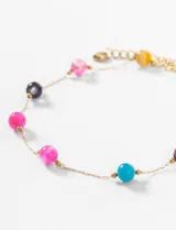 Tobillera de acero dorada con cuentas de piedra de colores engarzadas.
