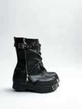 Botas de cuero negro con caña media, plataforma track y cierre de cremallera lateral. Presentan una correa con hebilla y ojales en la parte superior de la caña.