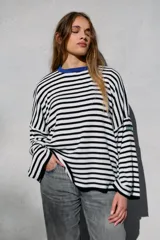 Sweater oversize de punto con diseño a rayas horizontales en blanco y negro, cuello redondo en color azul vibrante y mangas largas amplias. Presenta un pequeño parche decorativo en la manga.