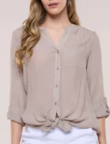Blusa de calce relajado color salmón, confeccionada en tela liviana con textura sutil. Presenta escote en V con abotonadura frontal, bolsillo parche en el pecho, mangas largas regulables con presilla y ruedo con opción de anudar en el frente.