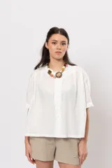 Camisa corta color blanco de corte amplio, con mangas cortas y sutiles detalles de volados a lo largo de la botonadura frontal.