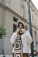 Bufanda tejida a mano en crochet, con capucha y diseño de cuadrados en tonos beige, marrón y negro.