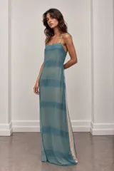 Vestido largo fluido de gasa translúcida en tono azul agua con estampado de franjas horizontales. Presenta escote recto, tirantes finos y caída amplia.