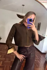 Camisa corta marrón de cuero ovino desgastado, con cuello clásico, cierre frontal con botones, mangas largas con cutouts y puños anchos dorados.