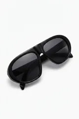 Lentes de sol con armazón negro de diseño envolvente y estilo aviador, con micas oscuras.
