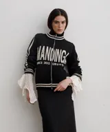 Campera tejida de algodón en color rojo, con cierre frontal completo, cuello alto y puños acanalados con detalles de rayas blancas. Presenta un diseño gráfico con texto blanco en el frente.