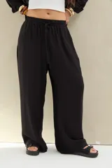 Pantalón largo negro de corte holgado, con cintura elástica fruncida y cordón ajustable delantero.