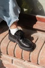 Zapato Oxford negro de cuero con cordones, suela track y detalle de aplique con logo en la lengüeta.