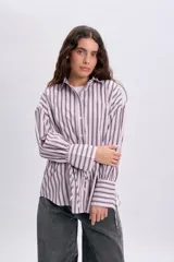 Camisa de manga larga con diseño de rayas verticales en tonos violeta y blanco, corte oversize, cuello camisero, cierre frontal con botones y detalles de lazos en el frente.