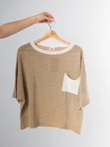 Remera tejida color crema con cuello redondo y bolsillo frontal verde.