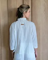 Camisa de manga tres cuartos color beige con cuello con volados y botones frontales. Presenta un detalle de color negro en la parte superior de las mangas.