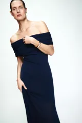 Vestido largo de punto color azul marino, con escote recto tipo off-shoulder con detalle de frunces en la parte superior. Presenta un diseño entallado en el torso y una falda con caída fluida y bajo combinado en tejido semitransparente.