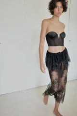 Falda midi semitransparente de tiro medio, confeccionada en tejido de encaje negro con detalle de superposición en la cintura y ajuste con lazada. Presenta bajo acabado en ondas y abertura en la espalda.