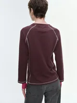 Remera de manga larga en tela waffle color negro, con costuras decorativas en contraste de color blanco. Presenta diseño de manga raglán y un pequeño bordado en el centro del pecho.
