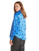 Camisa de satén de corte holgado con cuello camisero y cierre frontal de botones metálicos. Presenta un estampado de cuadrados negros sobre fondo azul vibrante, mangas largas con puños abotonados y un acabado brillante característico del satén.