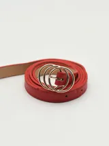 Cinto rojo de cuero sintético con hebilla dorada de doble aro entrelazado.