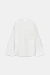 Camisa de cuello redondo y manga larga con puños anchos. Presenta un bolsillo de plastrón en el pecho con detalles de bordados a tono, los cuales también se encuentran en los puños. Cierre frontal con botones ocultos por tapeta.