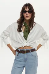 Camisa blanca de manga larga con flecos en la espalda y las mangas, confeccionada en mezcla de algodón, poliamida y elastano.